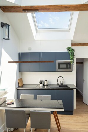 Eine moderne Küche mit Dachfenster, integrierten Geräten und einer Essecke mit Tisch und Stühlen.