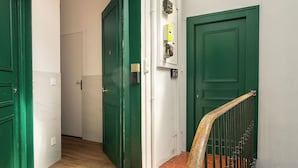 En hall med gröna dörrar, en trappa med ett träräcke och ett takfönster ovanför.