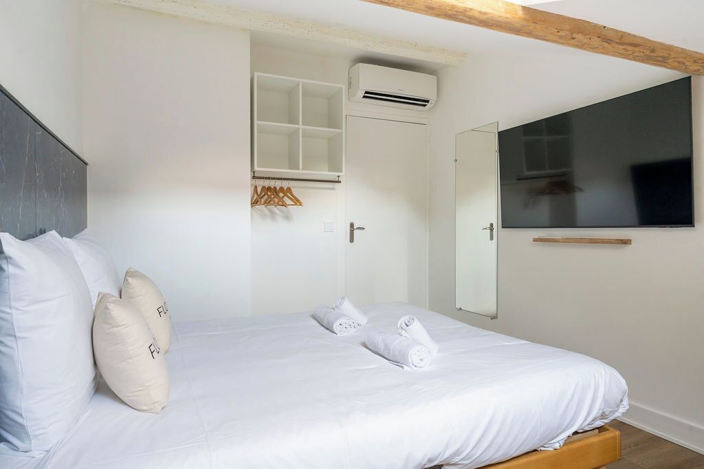 Une chambre à coucher comprenant un lit, des oreillers blancs, une tête de lit en bois, une armoire, un miroir et un appareil de climatisation.