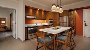 Una cocina moderna con gabinetes de madera, un refrigerador de acero inoxidable y una zona de comedor con una mesa y sillas blancas.