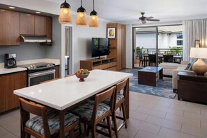 A modern kitchen with a dining area, a flat-screen TV, and a balcony with outdoor seating. - Beachfront Lahaina Resort: Spacious 2BR Oasis, Full Access & Snorkeling (Lahaina)