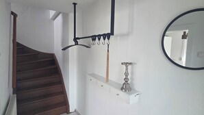 A staircase leading to a landing with a white wall, a black metal rack with hooks, a small shelf with a candle, and a round mirror. - Vacation Rental in the Heart of Gieselwerder (Wesertal)