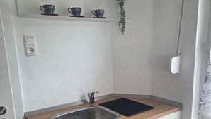 A compact kitchen with a sink, wooden countertop, and a shelf above holding cups and a plant. - Vacation Rental in the Heart of Gieselwerder (Wesertal)