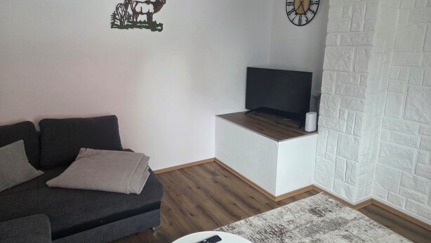 A living room with a sofa, a coffee table, a flat-screen TV, a clock, and a decorative wall piece. - Vacation Rental in the Heart of Gieselwerder (Wesertal)
