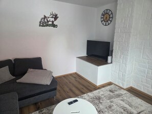 A living room with a sofa, a coffee table, a flat-screen TV, a clock, and a decorative wall piece. - Vacation Rental in the Heart of Gieselwerder (Wesertal)