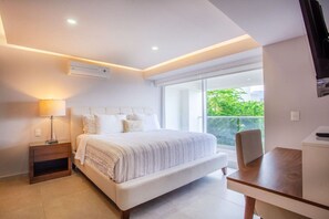 Ein modernes Schlafzimmer mit einem großen Bett, einem Nachttisch, einer Lampe und Blick auf Grün durch eine Schiebetür.