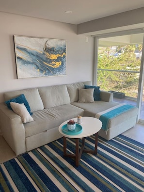 Un salon moderne avec un canapé d’angle beige, une table basse ronde et un grand tableau abstrait accroché au mur.