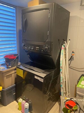 En kompakt tvättmaskin i mörk färg med en lucka på framsidan, en kontrollpanel med flera rattar och en liten hylla ovanför.