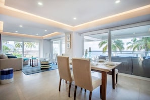 Un salon moderne avec un coin repas, de grandes fenêtres et une vue sur des palmiers.