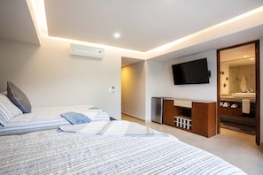 Une chambre d’hôtel moderne, équipée d’un lit, de tables de chevet, d’une télévision et d’une salle de bain visible à travers une porte ouverte.