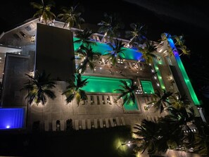 Ein modernes Gebäude mit Pool, Palmen und einer gut beleuchteten Außenfassade.
