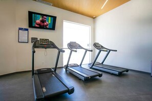Ett gym med tre löpband, en tv på väggen och en dörr som leder ut.
