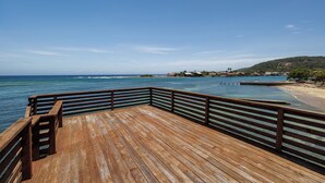 Eine Holzterrasse mit Geländer, die auf einen Strand und das Meer blickt.