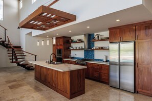 A modern kitchen with wooden cabinets, a central island, stainless steel appliances, and a staircase. - Spacious 4 bed 4 1/2 bath Beachfront home with pool (Islas de la Bahía)