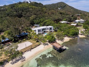 A modern house with a pool, surrounded by lush greenery and a beach.