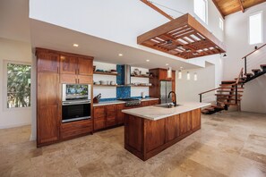A spacious kitchen with wooden cabinetry, a central island, and a staircase leading to an upper level.