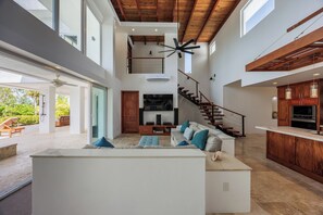 A spacious living area with a high ceiling, a built-in kitchen, and a staircase leading to an upper level.