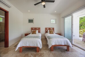A bedroom with two beds, a ceiling fan, and a sliding glass door leading to an outdoor area. - Spacious 4 bed 4 1/2 bath Beachfront home with pool (Islas de la Bahía)