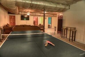 Une table de ping-pong dans une pièce équipée d’un canapé, d’un téléviseur et d’un coin bar.