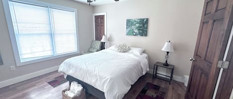 Une chambre à coucher avec un lit, une fenêtre, une porte, une table de chevet et un ventilateur de plafond.
