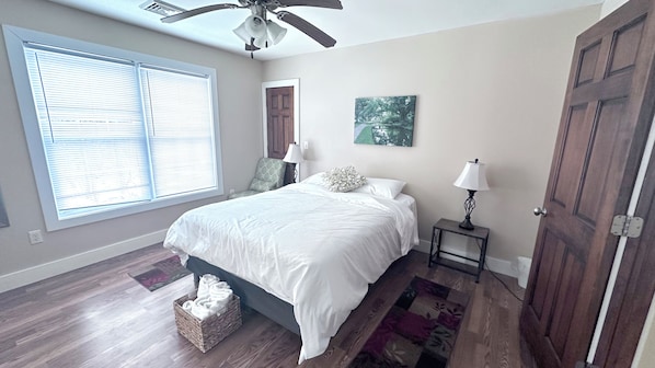 Une chambre à coucher avec un lit, une fenêtre, une porte, une table de chevet et un ventilateur de plafond.