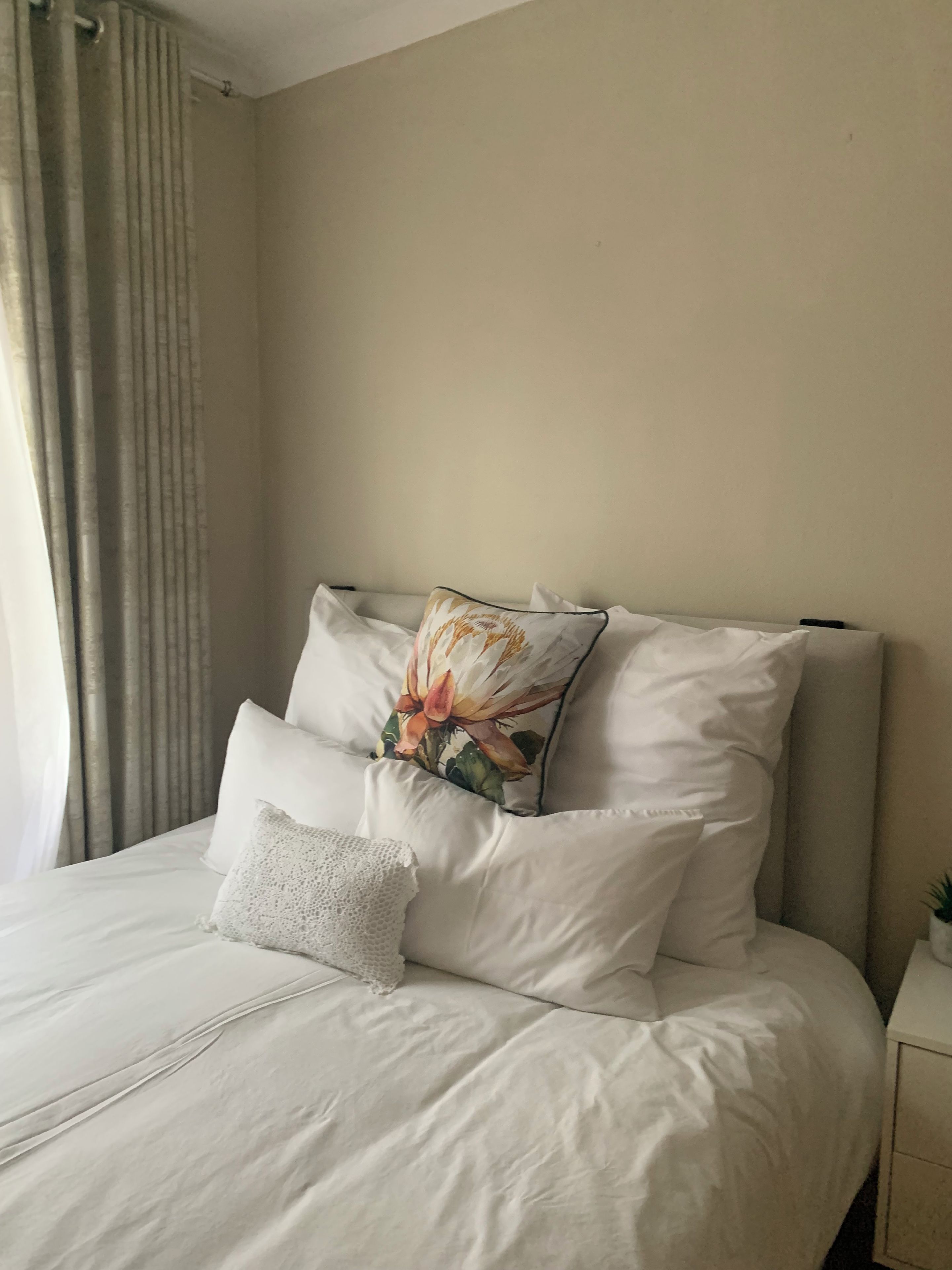 A neatly made bed with white linens, a decorative pillow with a floral design, and a plain pillow.