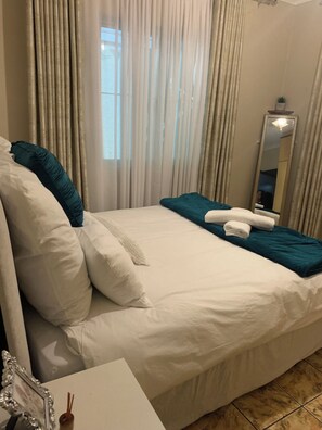 A hotel room with a bed, a mirror, and a window with curtains.