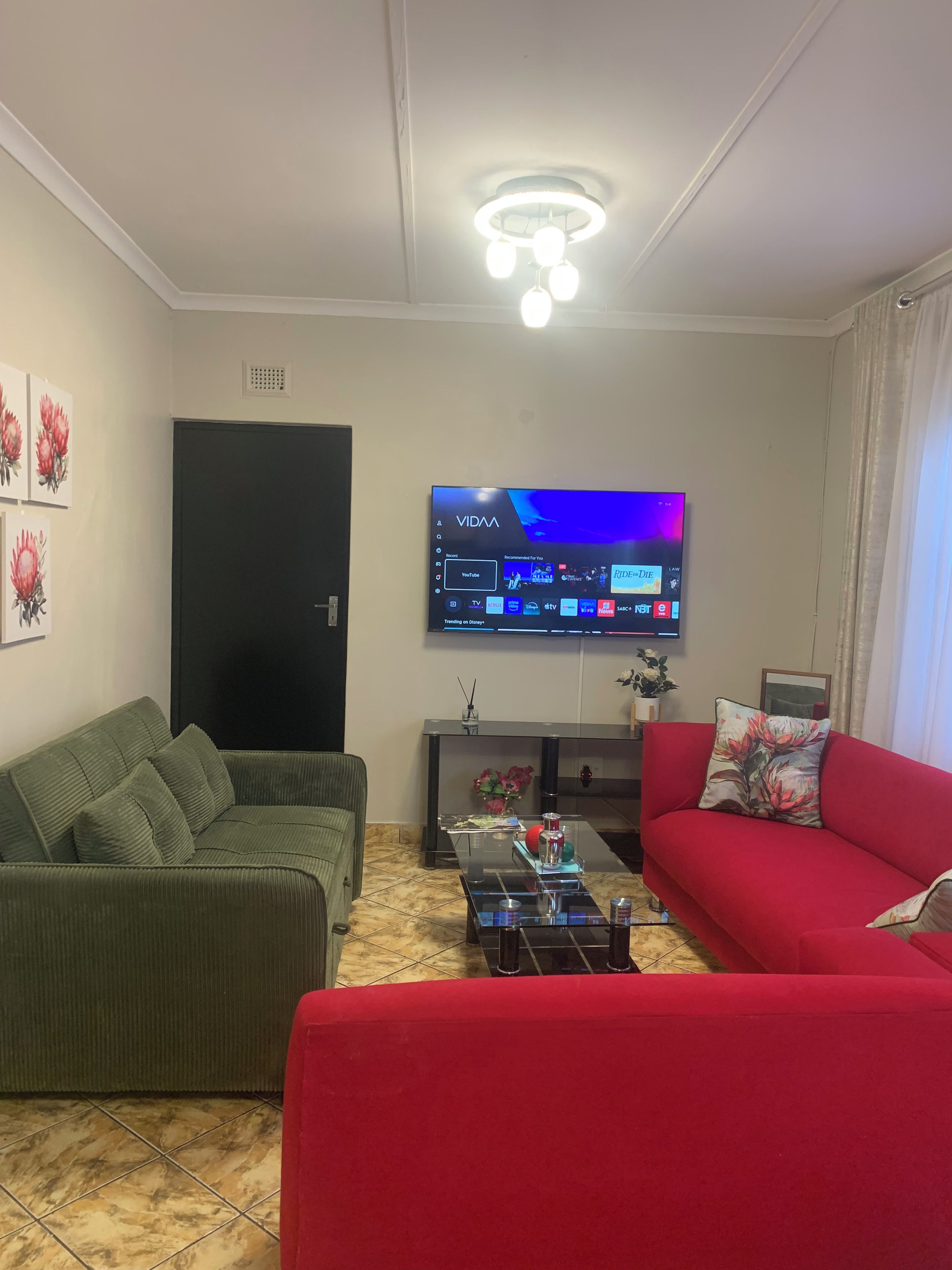 Una sala de estar con un televisor de pantalla plana montado en la pared, un sofá verde, un sofá rojo y una mesa de centro con adornos.