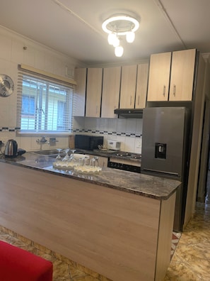 A modern kitchen with a central island, stainless steel appliances, and wooden cabinetry. - Cosy guest house (Durban)