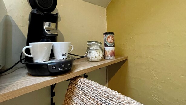A small kitchenette with a coffee maker, two cups, a jar of sugar, and a box of creamer on a shelf. - Cityflats Bruges (Bruges)