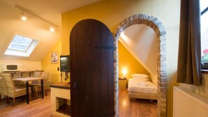 A room with a stone archway, a wooden door, a bed, a desk with a chair, and a skylight. - Cityflats Bruges (Bruges)