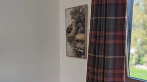 Een kamer met een eettafel, stoelen, een radiator, een raam met geruite gordijnen en een schilderij aan de muur.