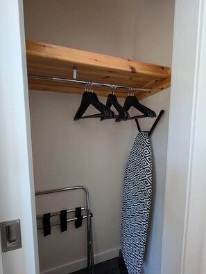 A small closet with a wooden shelf, a hanging rack, and an ironing board. - Culmill Lodges - Birch | Hot Tub Retreat near Loch Ness (Kiltarlity)