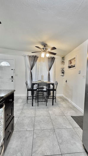 A compact kitchen with a dining table, chairs, a ceiling fan, and a white door. - Beautifully Renovated Home with Fenced Yard and Gazebo in a Prime Location (Pinellas Park)