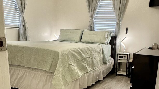A bedroom with a bed, a ceiling fan, a nightstand, a desk, and a TV mounted on the wall. - Beautifully Renovated Home with Fenced Yard and Gazebo in a Prime Location (Pinellas Park)