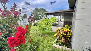 A garden with various plants and flowers, a white fence, and a building with a covered porch. - Beautifully Renovated Home with Fenced Yard and Gazebo in a Prime Location (Pinellas Park)