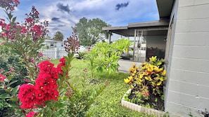 A garden with various plants and flowers, a white fence, and a building with a covered porch. - Beautifully Renovated Home with Fenced Yard and Gazebo in a Prime Location (Pinellas Park)