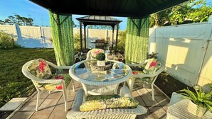 An outdoor patio with wicker furniture, a glass-top table, and a gazebo. - Beautifully Renovated Home with Fenced Yard and Gazebo in a Prime Location (Pinellas Park)