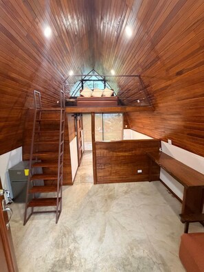 Ein Schlafzimmer im Stil eines Lofts mit schrägem Holzboden, einem Hochbett, einer Strickleiter und einer kleinen Schreibtischzeile.