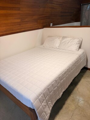 Ein Zimmer mit einem Einzelbett, einem Holz-Kopfteil, weißer Bettwäsche und einem Betonboden.