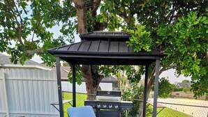 An outdoor patio with a table and chairs, a grill, and a pergola. - Villa Turtle View right on the water (Cape Coral)
