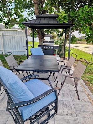Eine Terrasse im Freien mit Tisch, Stühlen, einem Grill und einer Pergola.