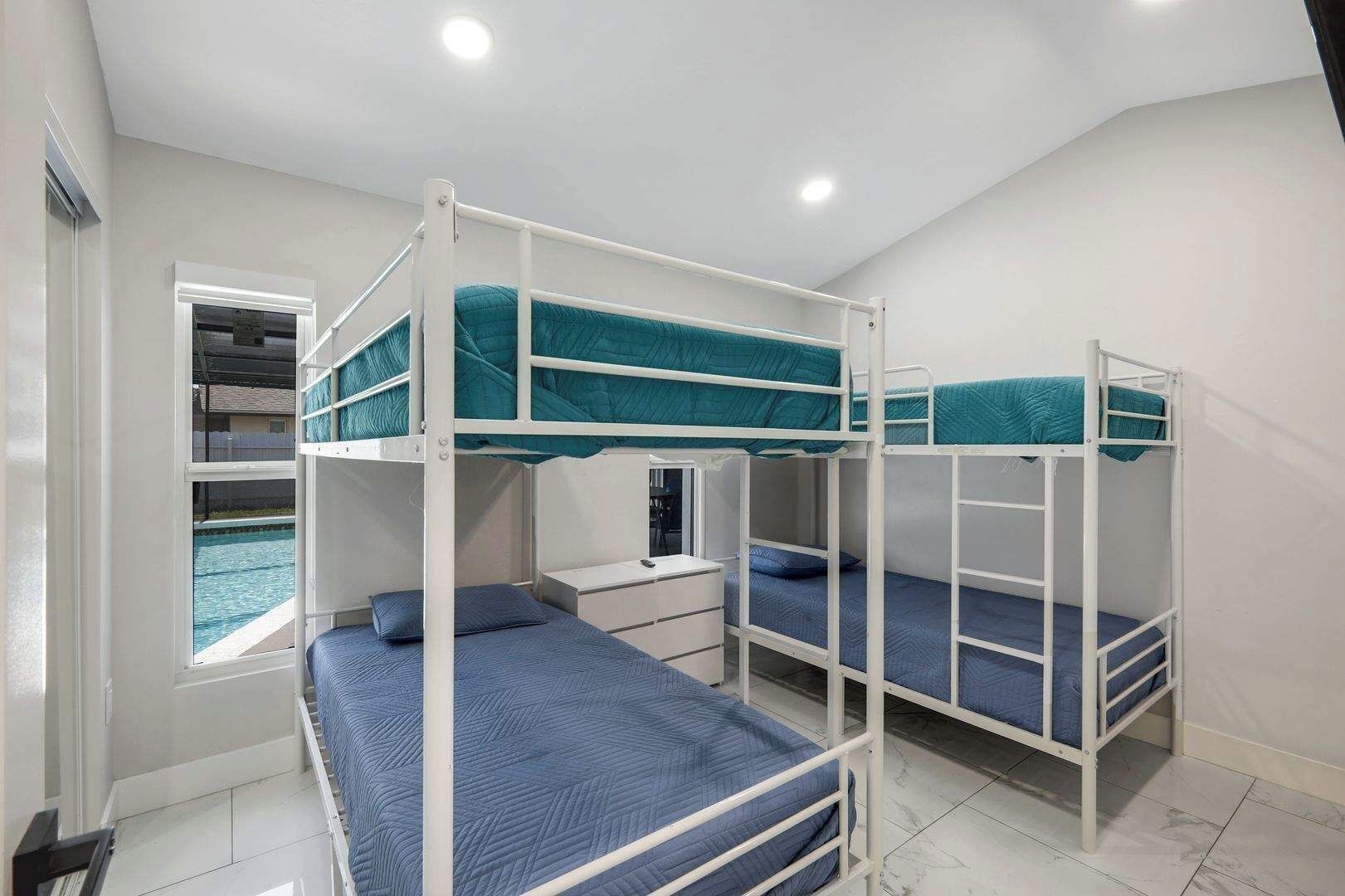 Una habitación con literas, una ventana con vista a una piscina y un escritorio con una silla.