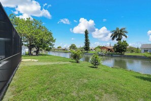A grassy area with a water body, trees, and a building in the background. - Villa Turtle View right on the water (Cape Coral)