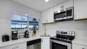 A modern kitchen with white cabinetry, a built-in dishwasher, a stove, and a microwave. - Villa Turtle View right on the water (Cape Coral)