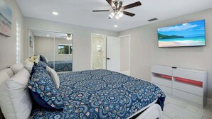 A bedroom with a bed, a ceiling fan, a TV, and a bathroom door. - Villa Turtle View right on the water (Cape Coral)