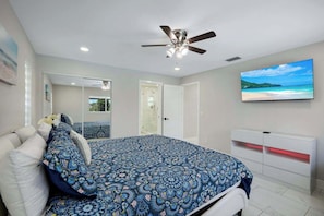Ein Schlafzimmer mit einem Bett, einem Deckenventilator, einem Fernseher und einer Badezimmertür.