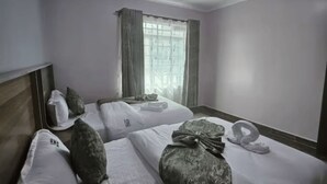 A hotel room with two beds, a window with curtains, a wooden headboard, and a towel on the floor. - Charming 2-bedroom apartment in enjoyable Naivasha getaway (Naivasha)