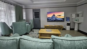 A hotel room with a sofa, chairs, a TV, a small table, a water dispenser, and a sink. - Charming 2-bedroom apartment in enjoyable Naivasha getaway (Naivasha)