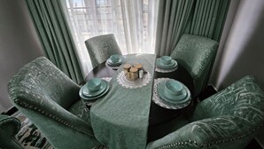 A dining area with a round table, green upholstered chairs, and a lace table runner. - Charming 2-bedroom apartment in enjoyable Naivasha getaway (Naivasha)